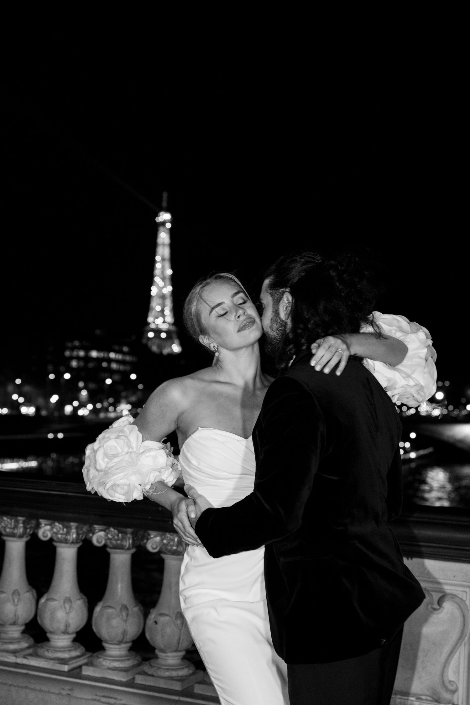 A romantic black and white wedding photo series showing a couple posing at night with city lights in the background.