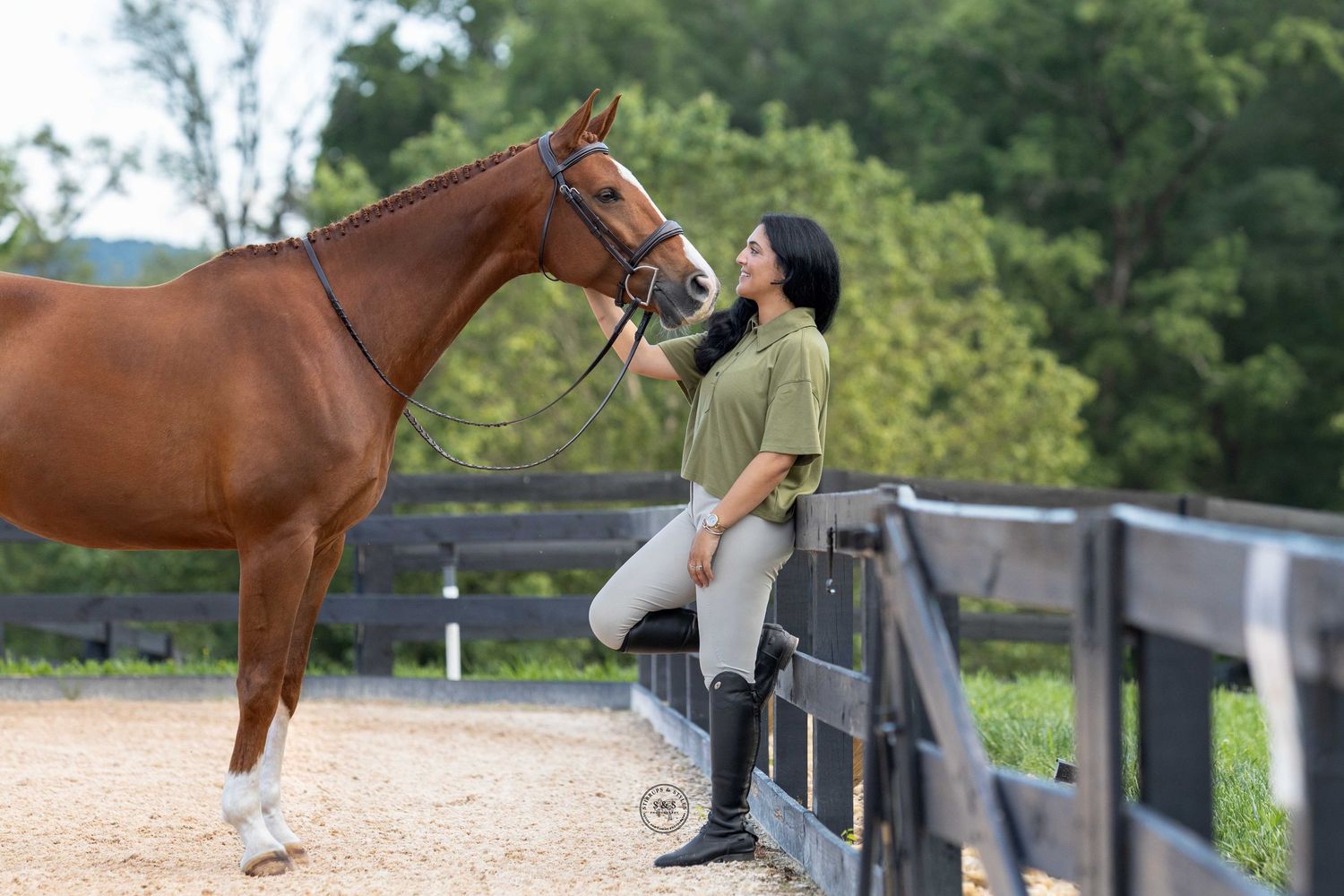 A chestnut horse being led along a wooden fence at an equestrian facility on a sunny day.