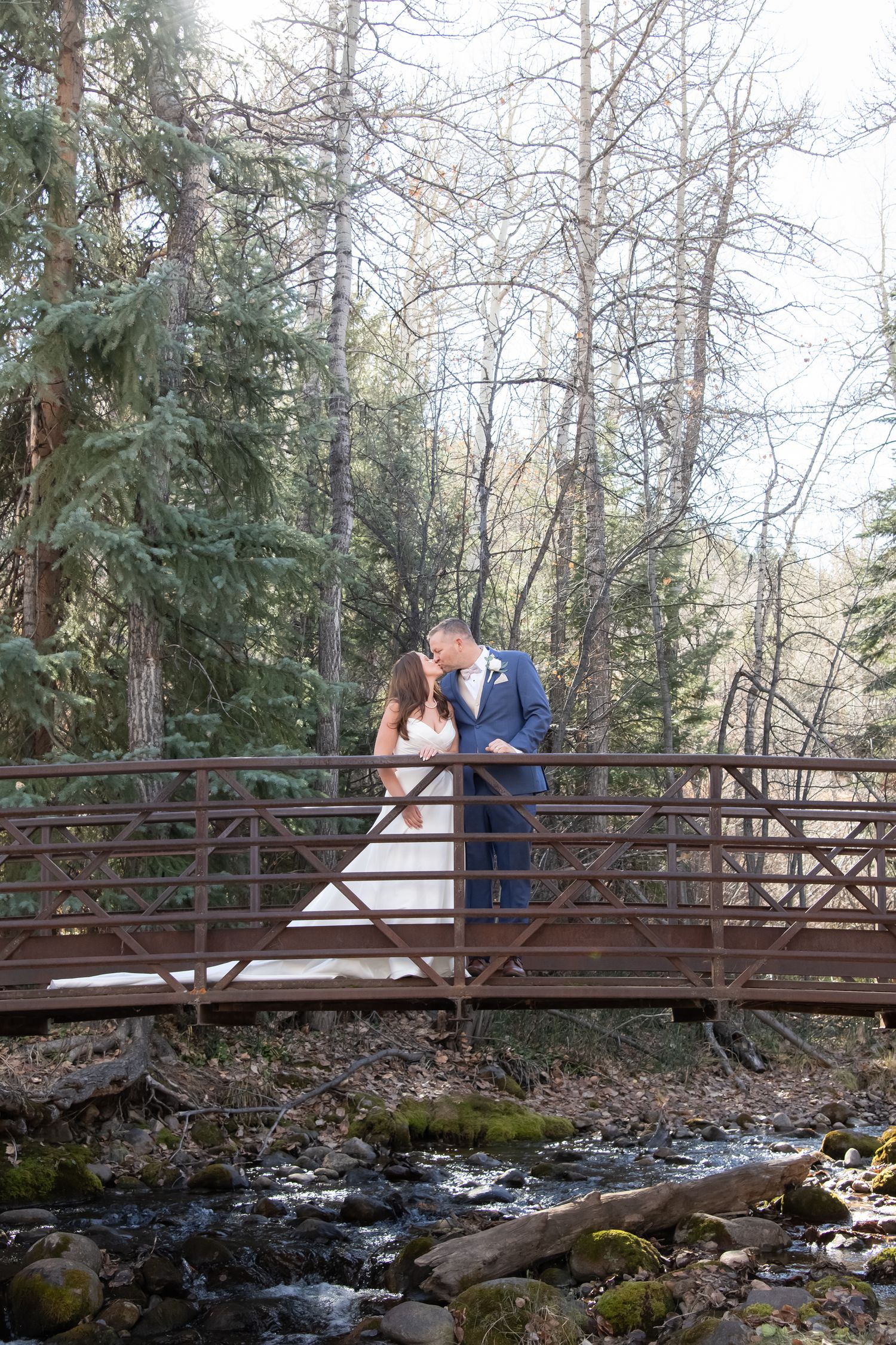 Bride and groom kiss on a little bridge over a creek after their wedding at The Beaver Creek Chapel.