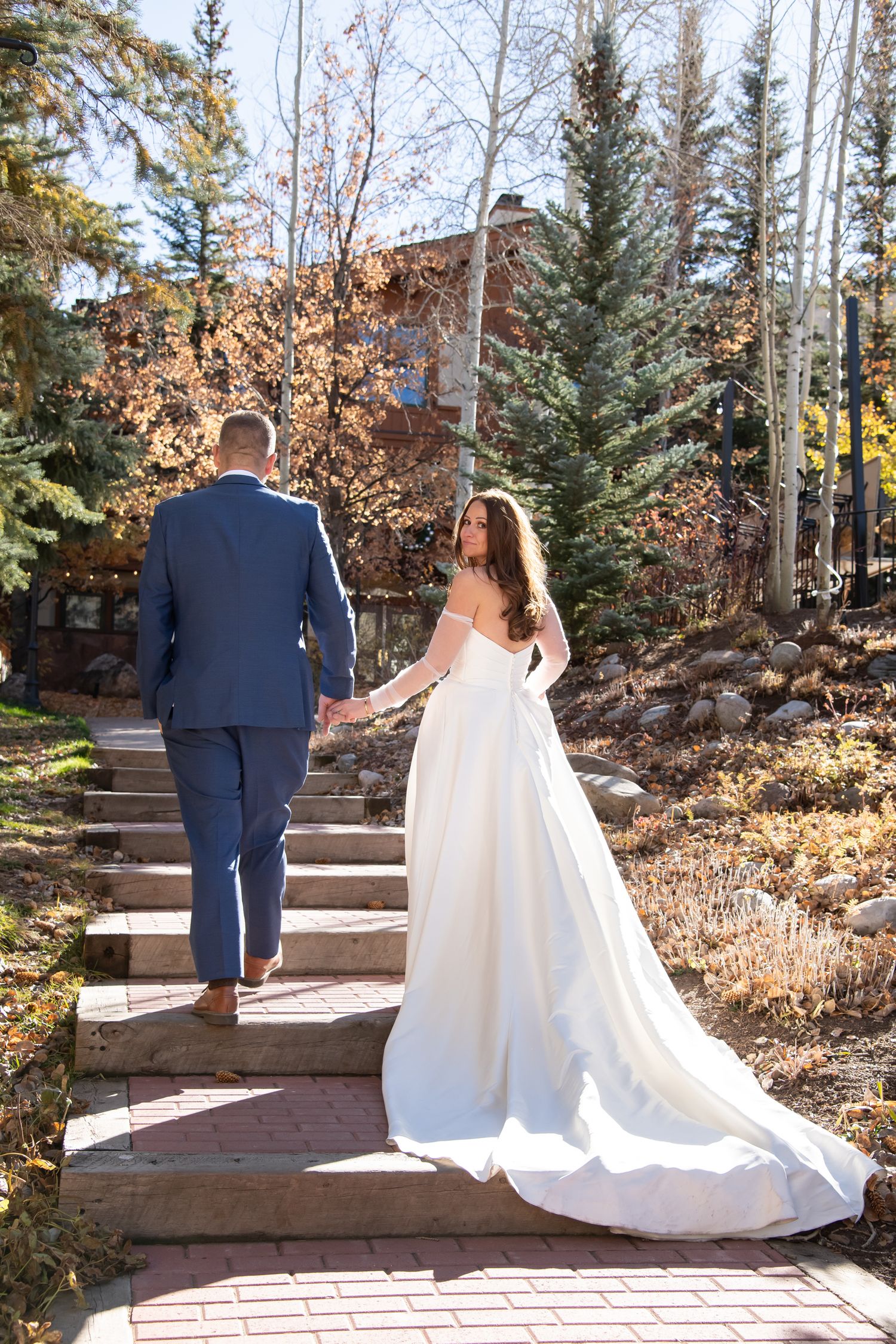 Elegant photo of bride and groom walking up a staircase with her dress trailing behind her down the stairs in Vail Colorado wedding