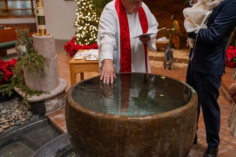 A baptismal font with water surrounded by participants during a religious ceremony.