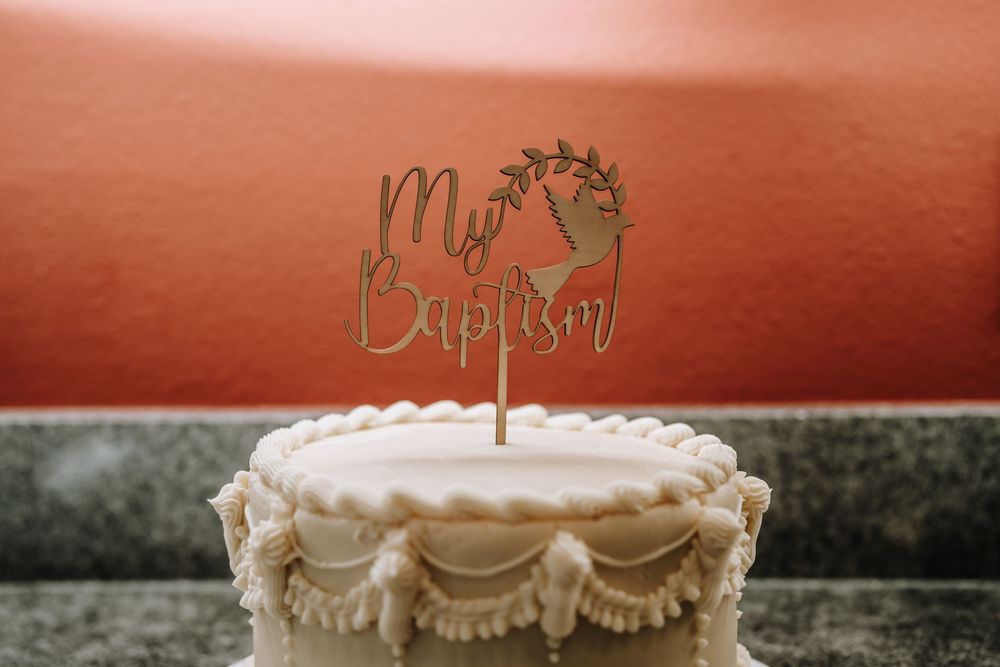 White baptism cake with decorative frosting and elegant topper displayed on granite countertop.