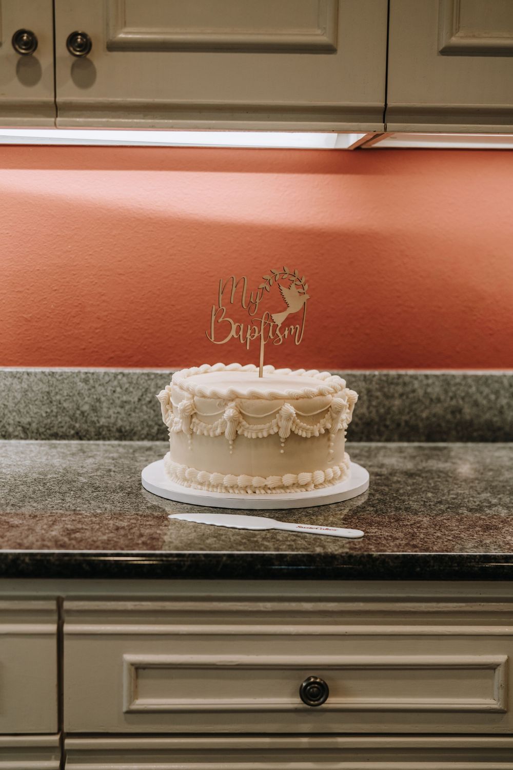 Elegant white baptism cake with ornate details displayed on a granite counter.
