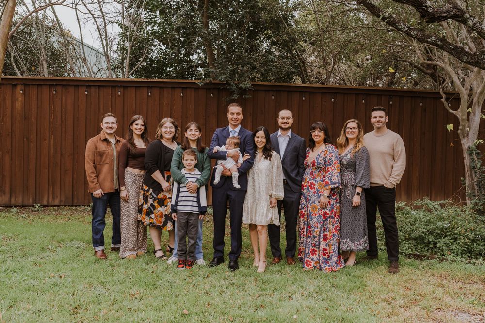 Extended family group portrait of multiple generations gathered in backyard with wooden fence.