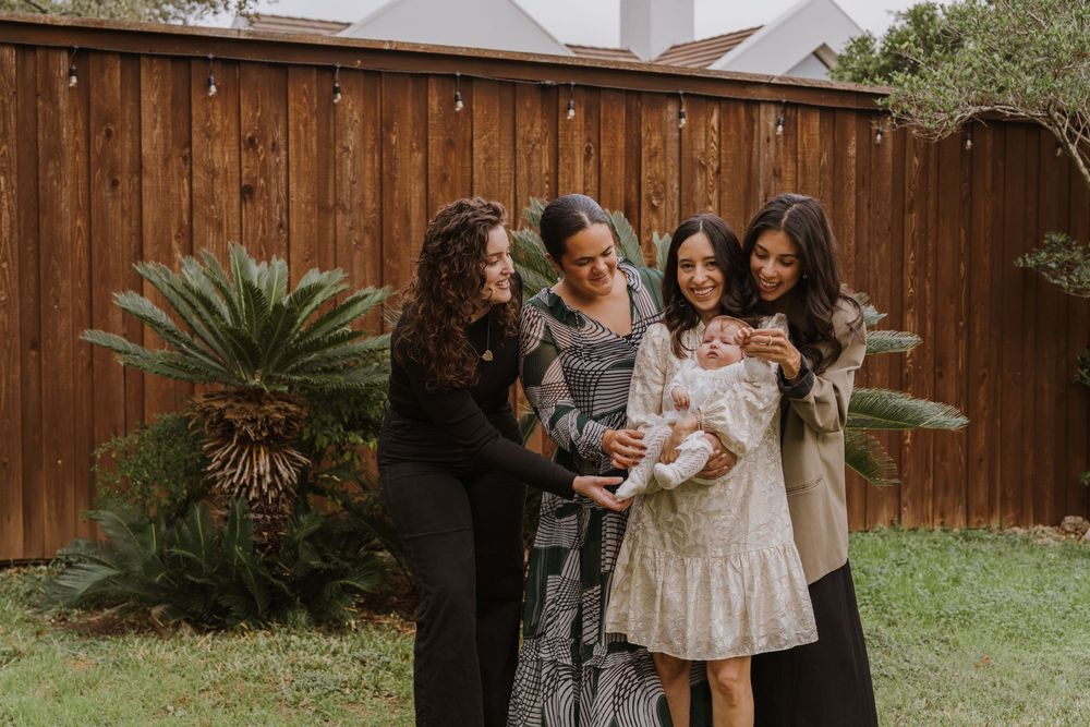 A group gathers in a backyard with wooden fence and palm plants to celebrate a special occasion.