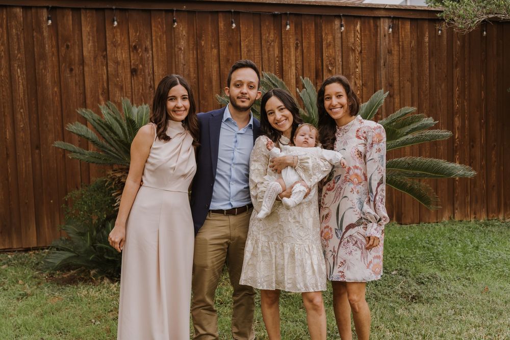 Small group poses together in coordinated formal attire in front of wooden fence and palm plants.
