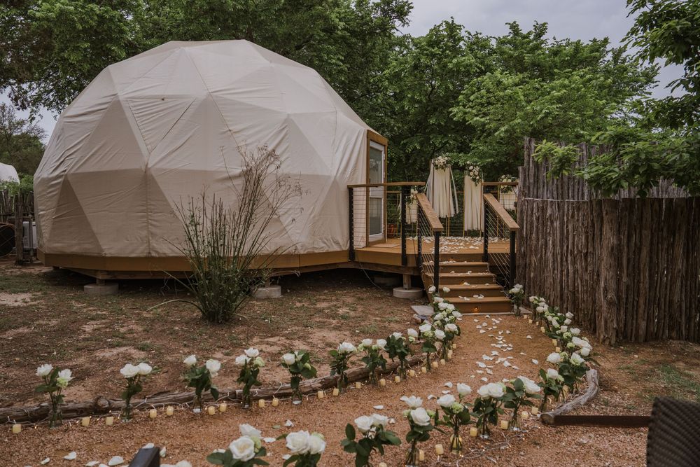 Large white tent structures set up in a backyard garden space for an outdoor event.
