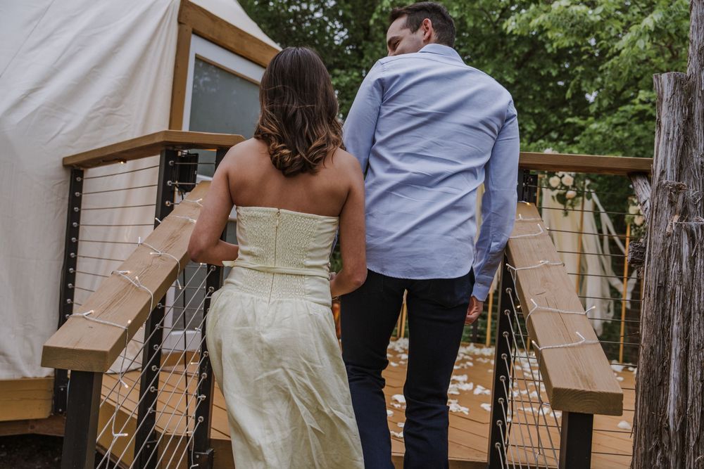 A couple shares an intimate moment in an outdoor garden setting with white drapes and greenery.