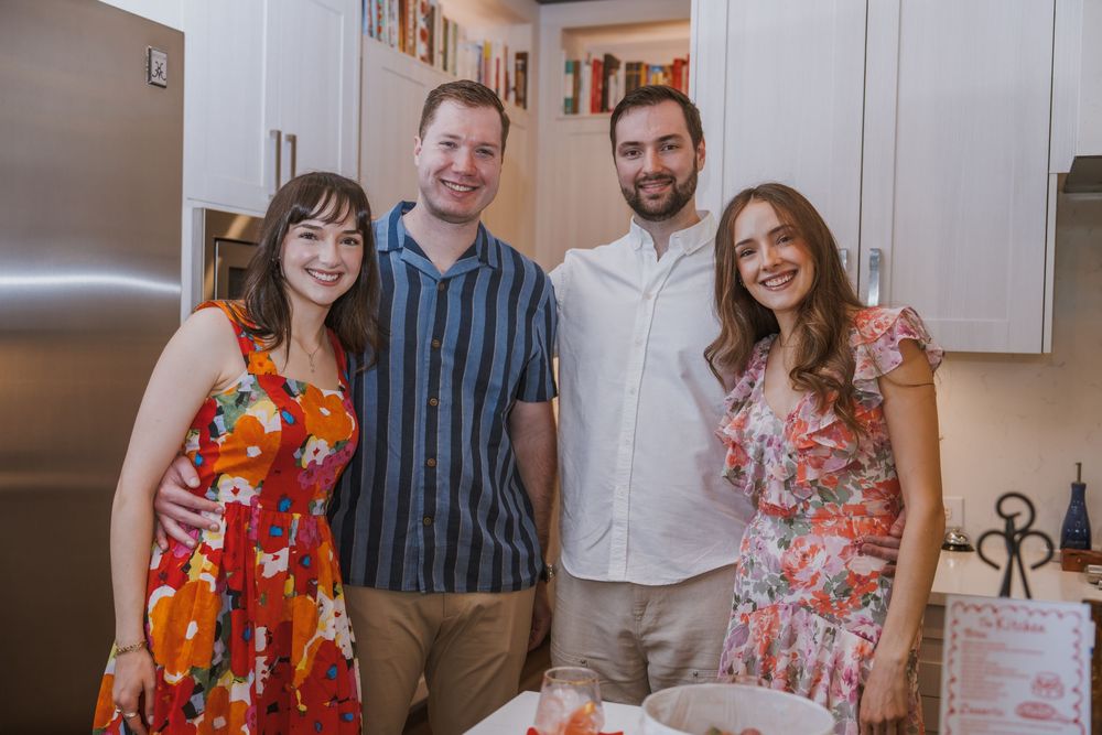 Four people gather together in a modern white kitchen wearing colorful summer attire.