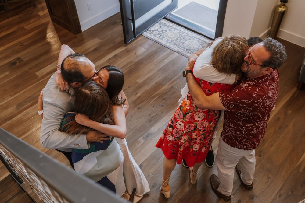 Two couples embrace in an emotional moment on hardwood floors indoors.