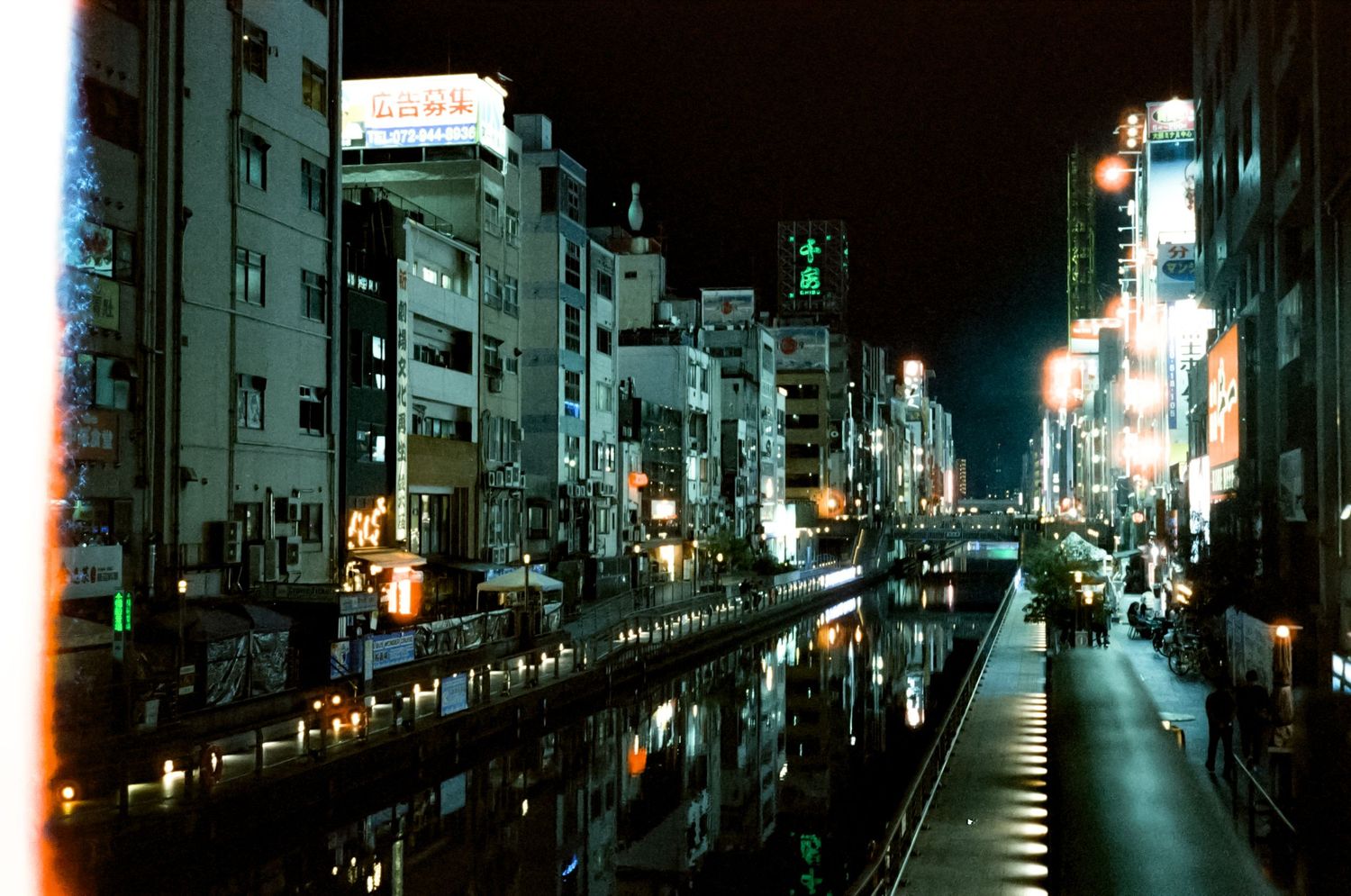 A dark city street at night with glowing lights and buildings illuminated along both sides of the road.