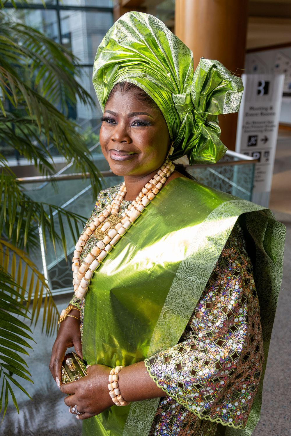 Traditional West African attire featuring bright green gele headwrap and dress with layered pearl necklaces and floral details.