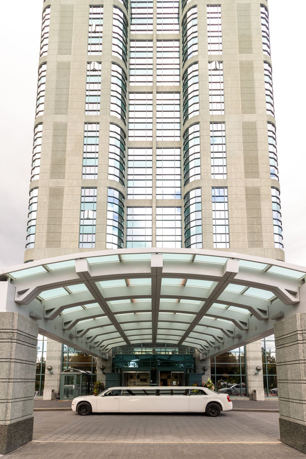 Modern curved glass entrance canopy with white bus parked outside a tall residential building complex.