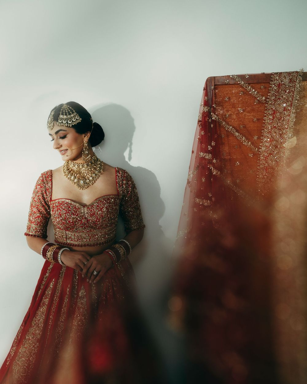 Traditional Indian bridal lehenga in deep red with intricate gold embroidery and detailed neckline displayed against neutral wall.