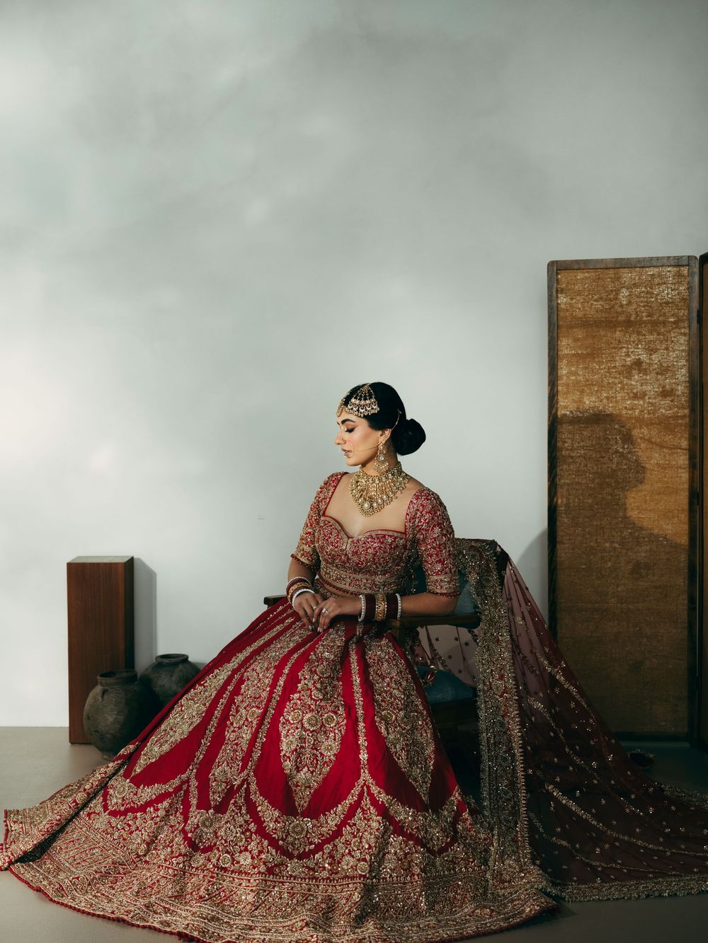 A traditional Indian bridal lehenga in deep red and gold embroidery photographed against a minimalist backdrop.