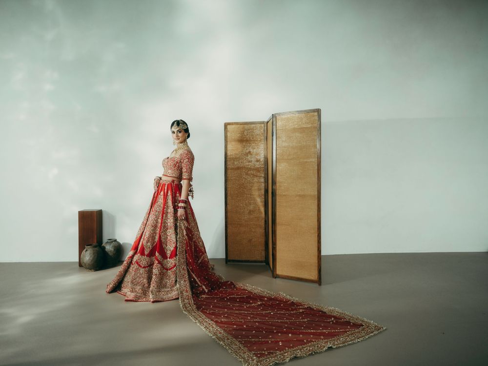 A figure in a red traditional gown sits elegantly on the floor against a minimalist backdrop with wooden doors.