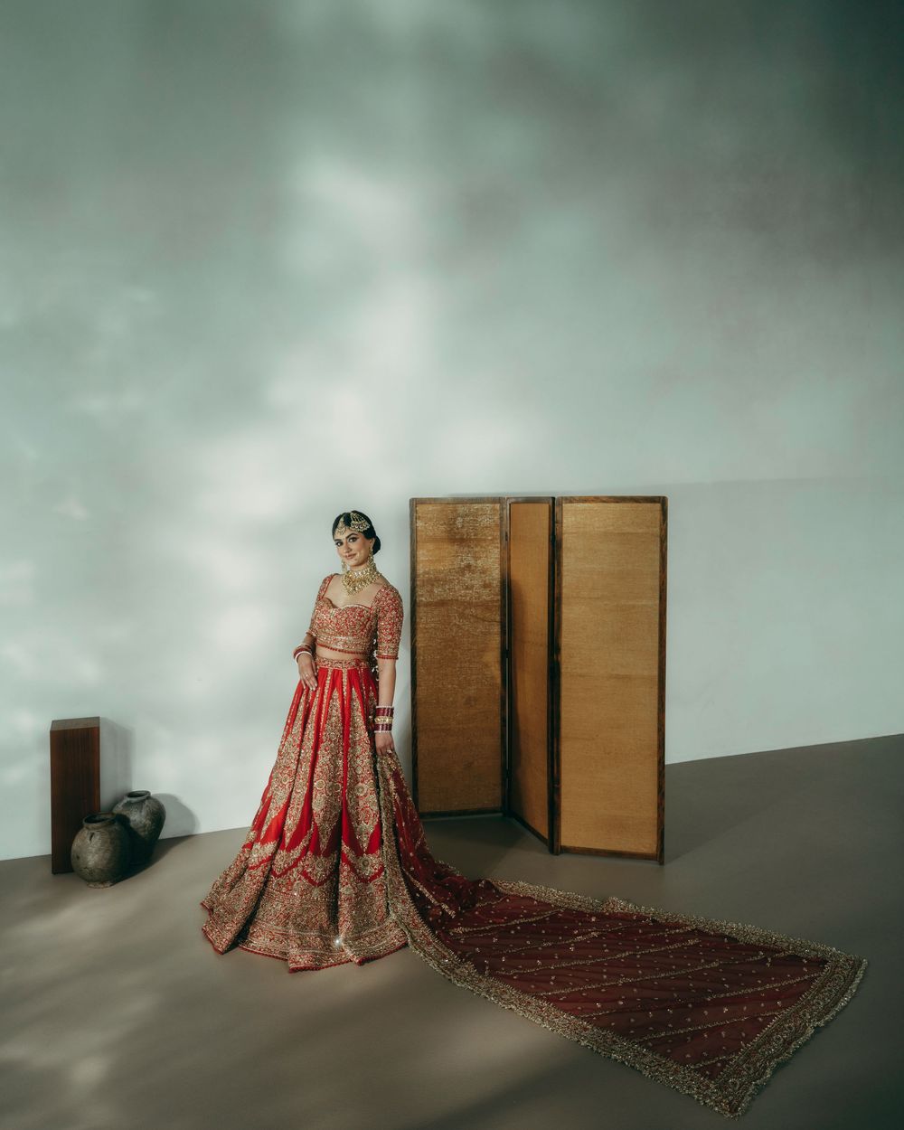 A traditional red and gold Indian bridal lehenga displayed on a mannequin against a moody green-tinted backdrop.