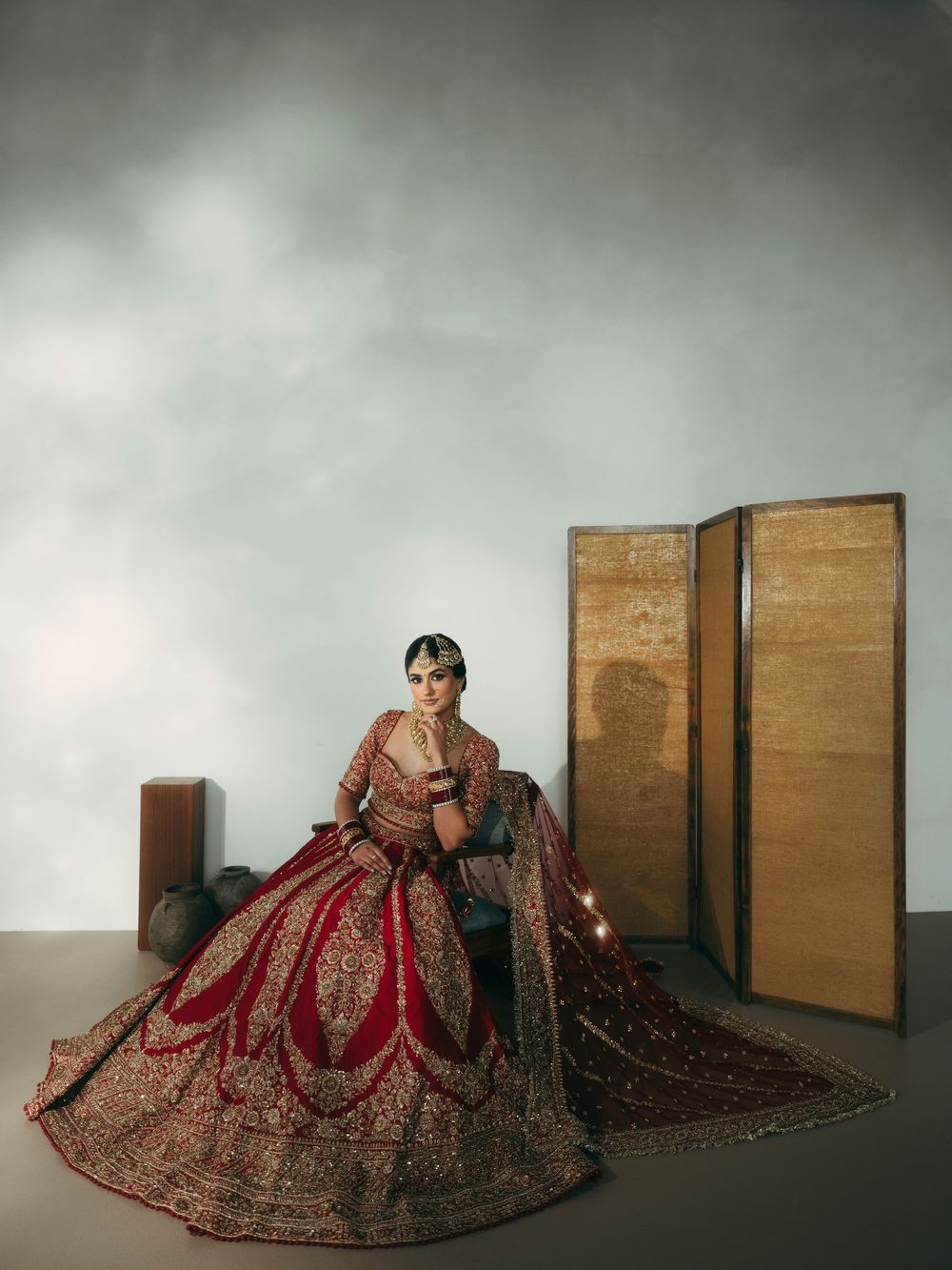 Traditional Indian bridal lehenga in deep red with intricate gold embroidery photographed against minimal studio backdrop.