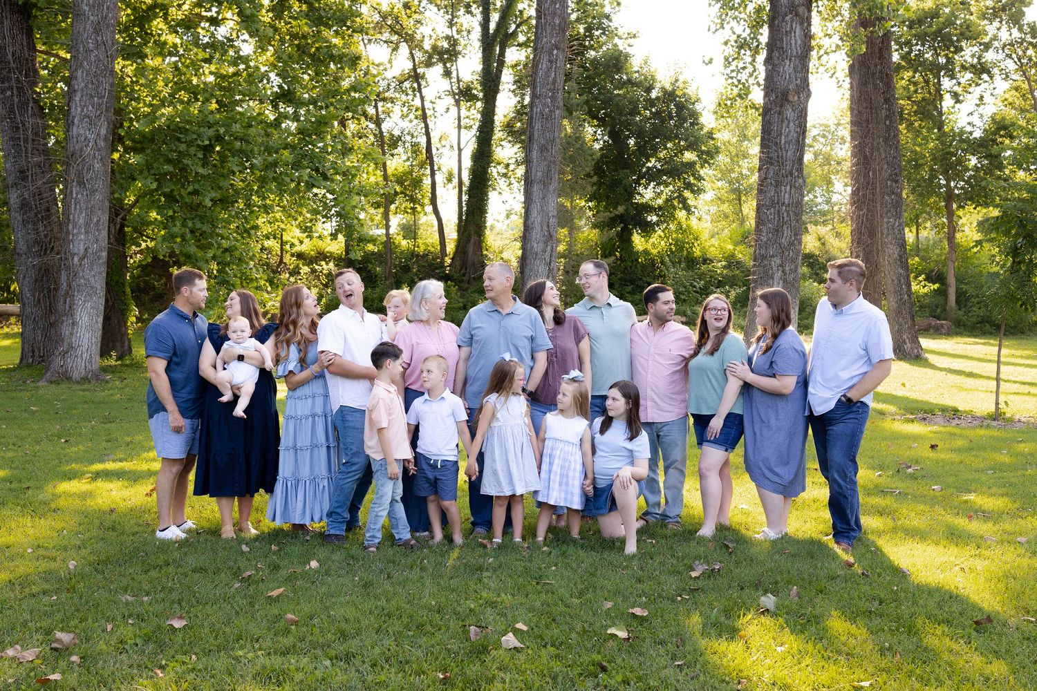A large family group gathers outdoors on a sunny day wearing coordinated blue and white outfits in a park setting.
