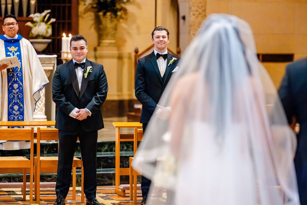 A traditional church wedding ceremony shows the groom waiting at the altar as the bride approaches in her flowing veil.
