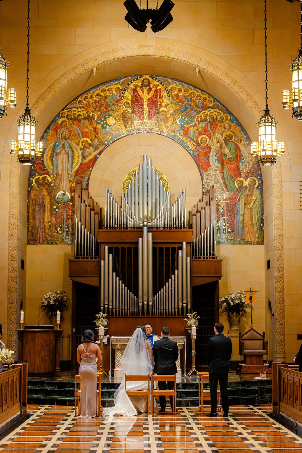 Wedding ceremony taking place in an ornate church sanctuary with organ pipes and decorative murals on the walls.