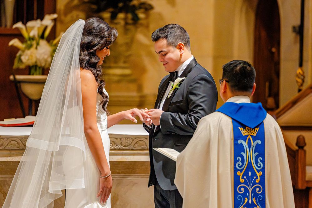 A couple exchanges rings during their traditional church wedding ceremony with blue and gold altar decor in the background.