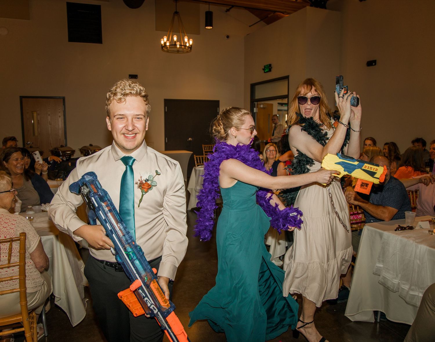 Wedding guests dance and play with colorful toy Nerf guns during a fun reception celebration.