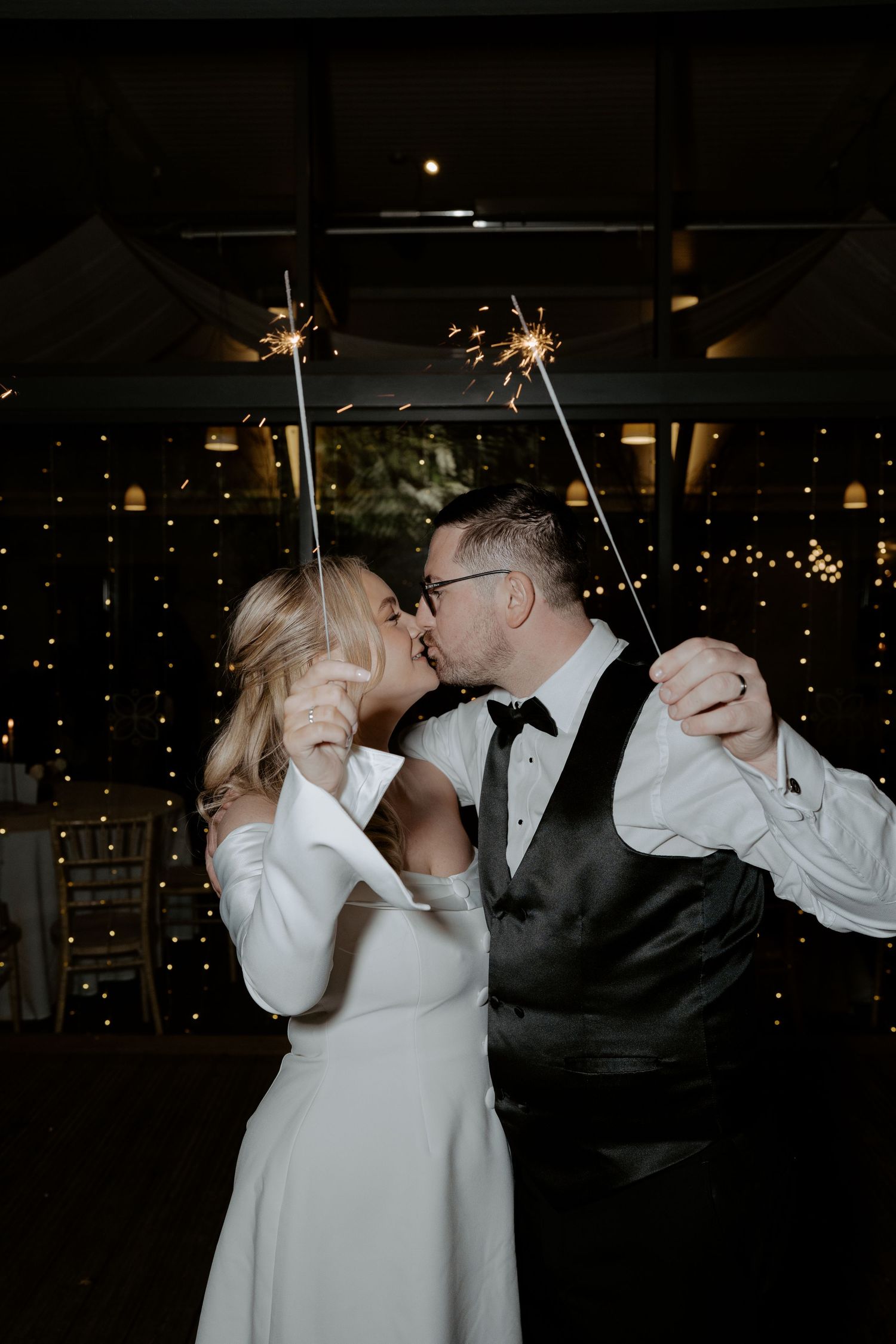 A couple stands in an arched brick doorway with rustic wooden doors opened wide on their wedding day.
