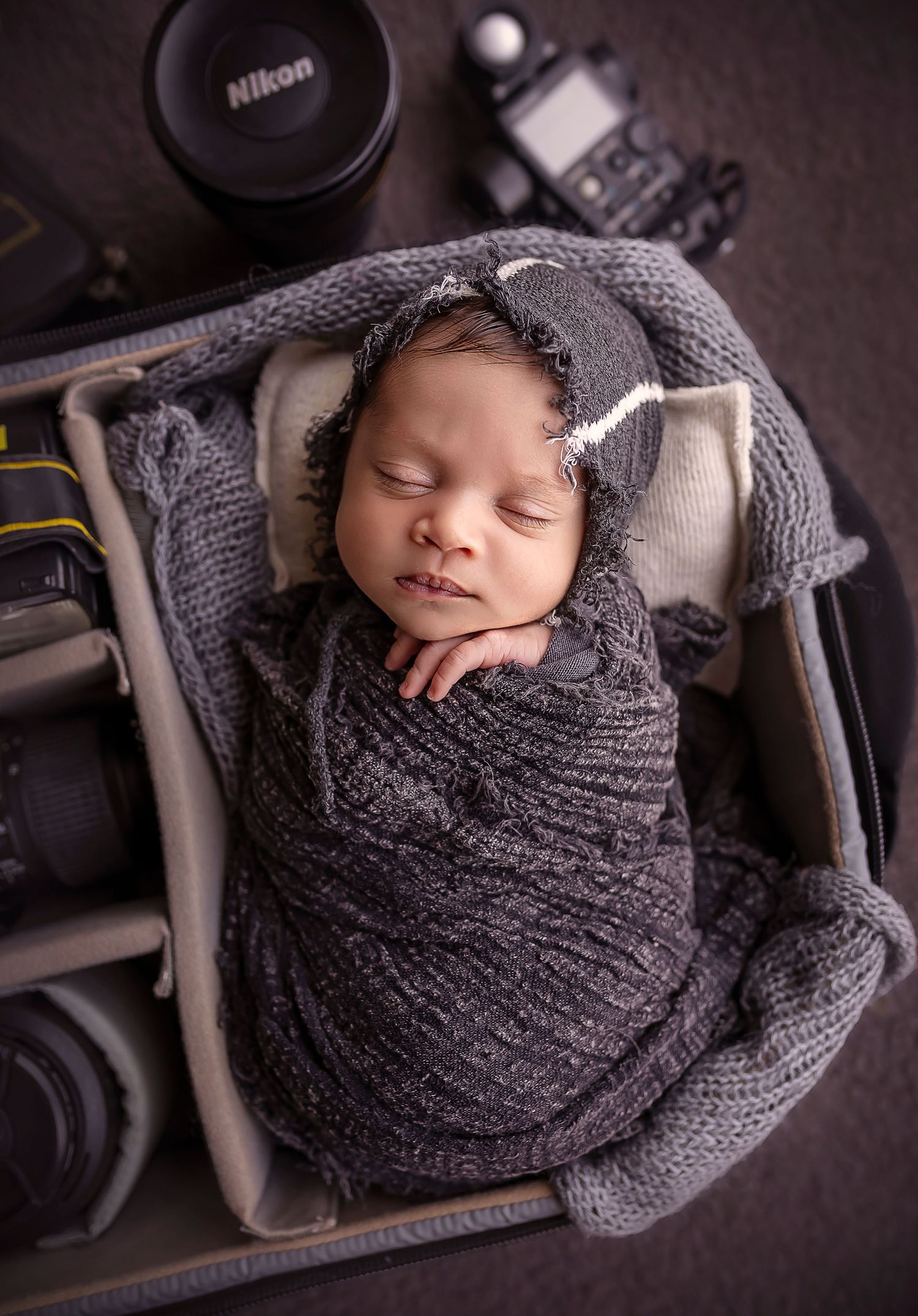 bebe envuelto en un pano negro con un gorrito de tela duerme tranquilamente dentro de un bulto para camaras