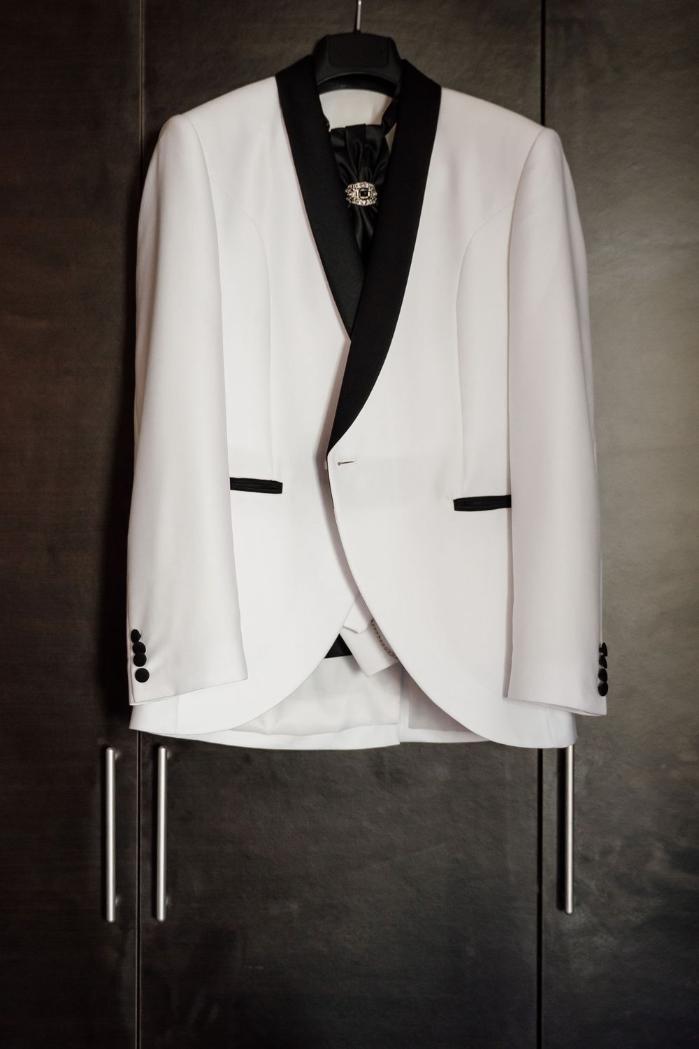 A white formal tuxedo jacket with black trim details hanging against a dark background.