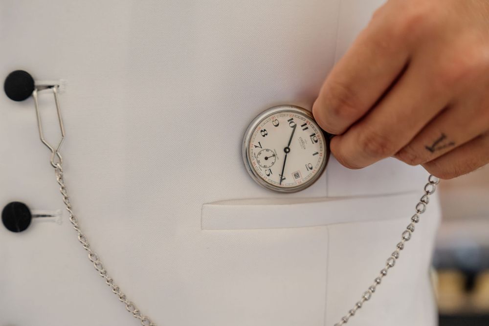 A hand holds a medical stopwatch against a white coat with chain attachments.