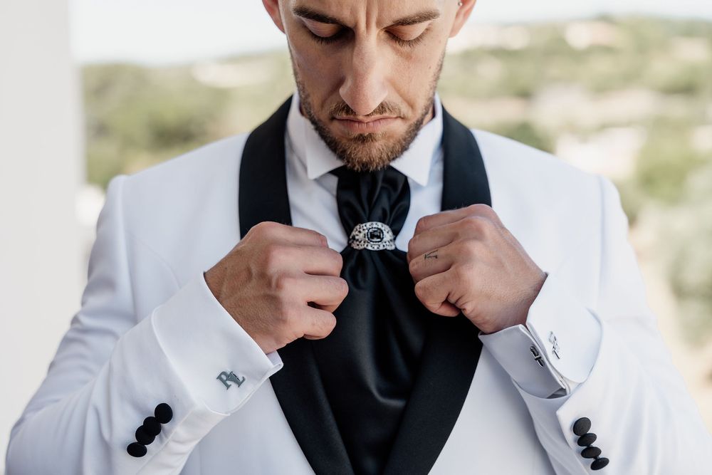 A close-up shot of someone adjusting a black bowtie while wearing a white tuxedo jacket.