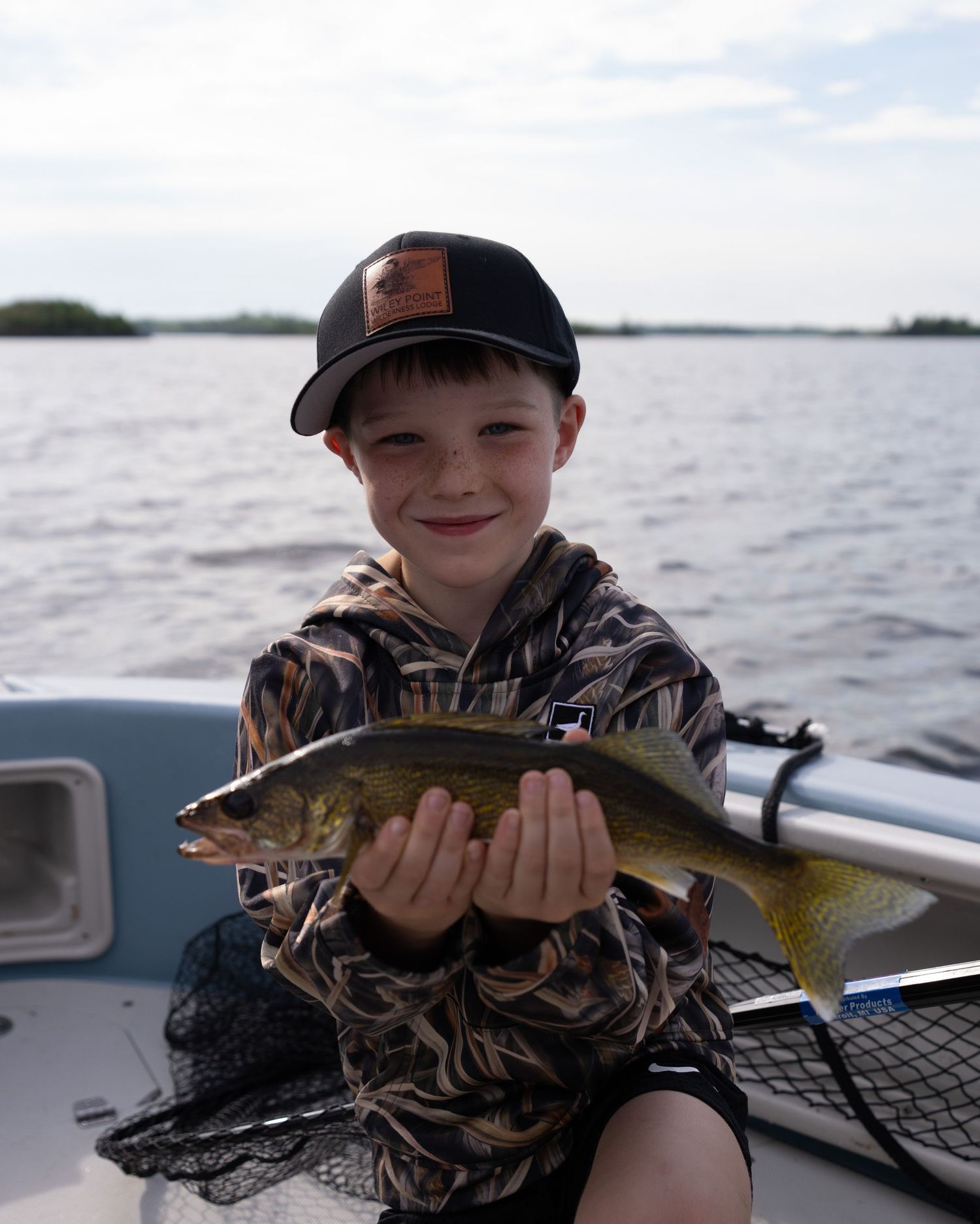 Young angler proudly displays freshly caught walleye fish on a boat.