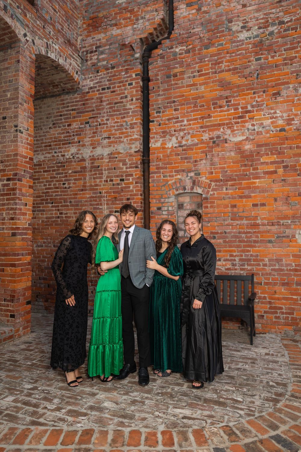 Formal group photo against brick wall with people in elegant green and black dresses.