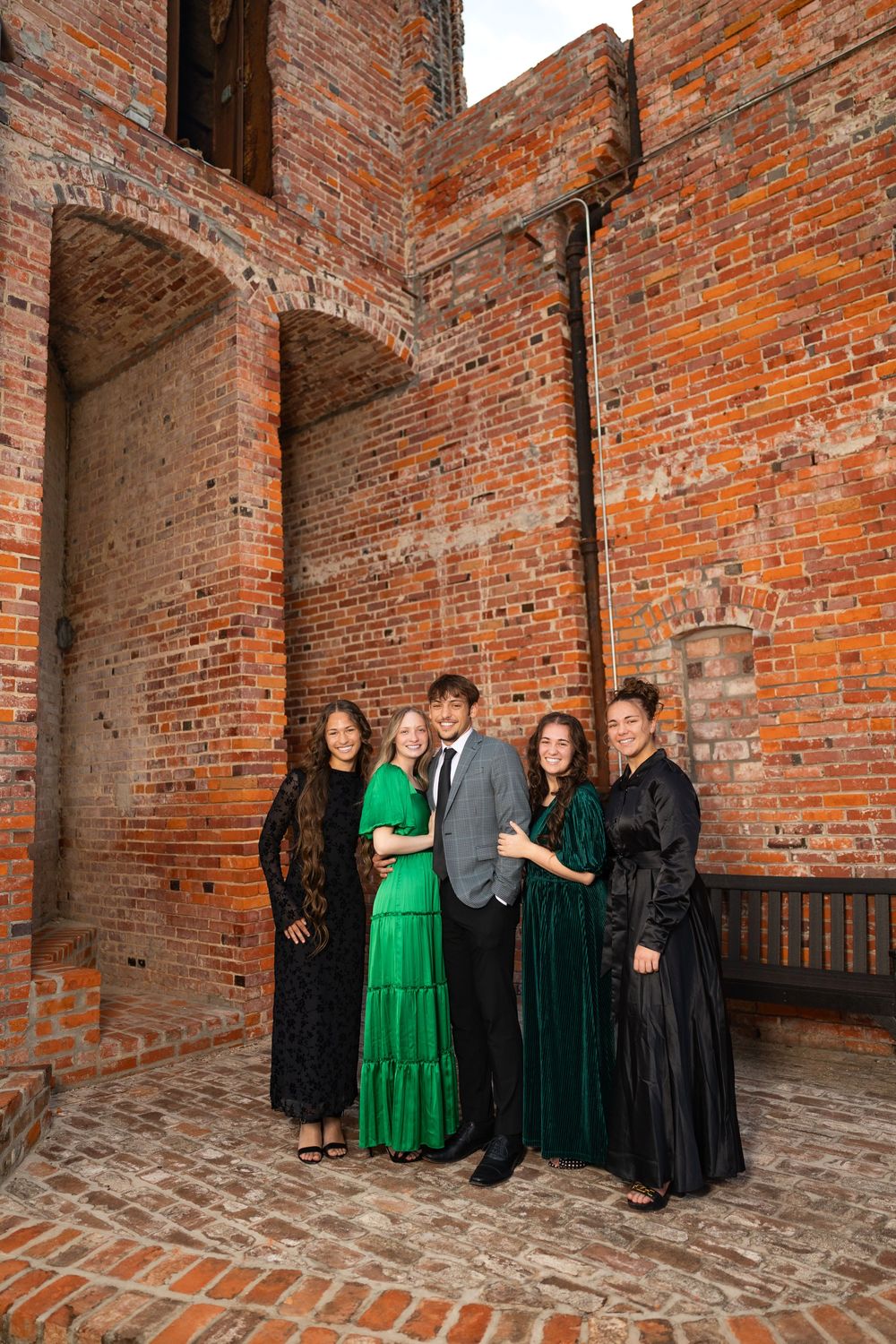 Group portrait in formal attire against rustic brick architecture.