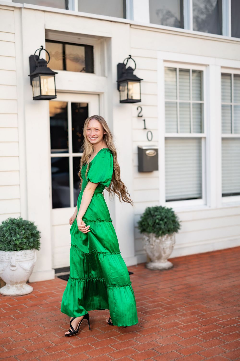 Woman in flowing green tiered maxi dress twirls on brick patio.