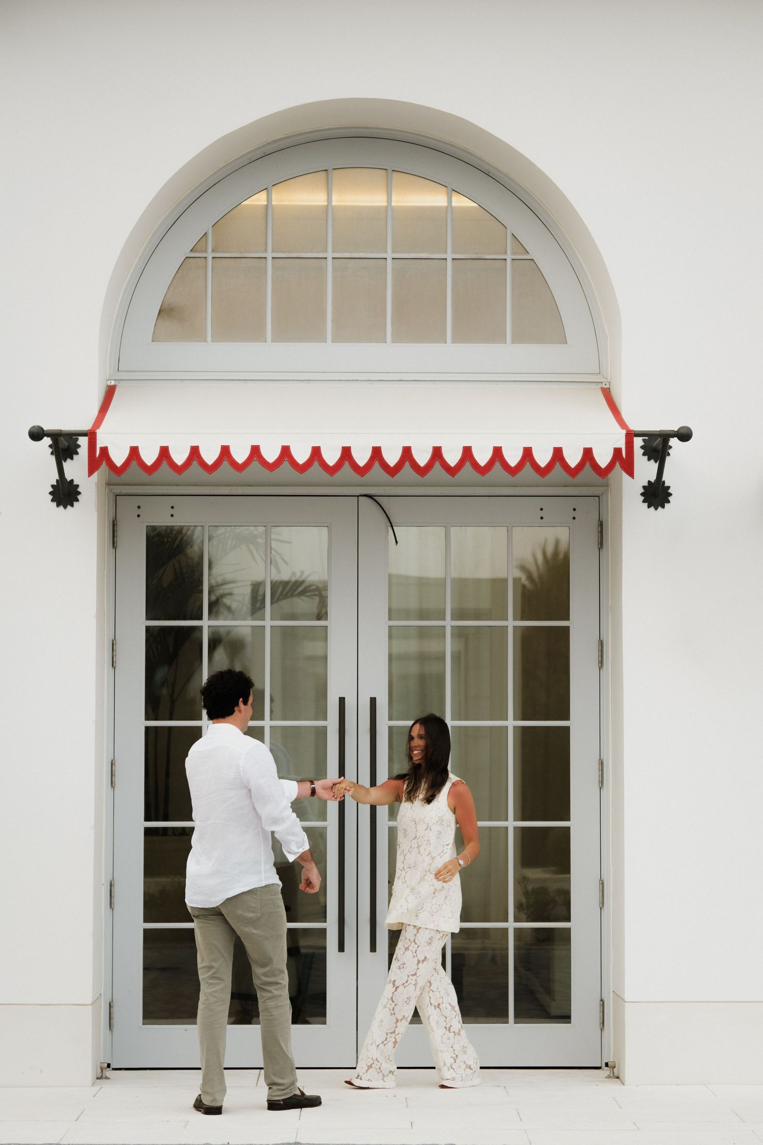 A couple entering through elegant double doors with an arched window and red awning.