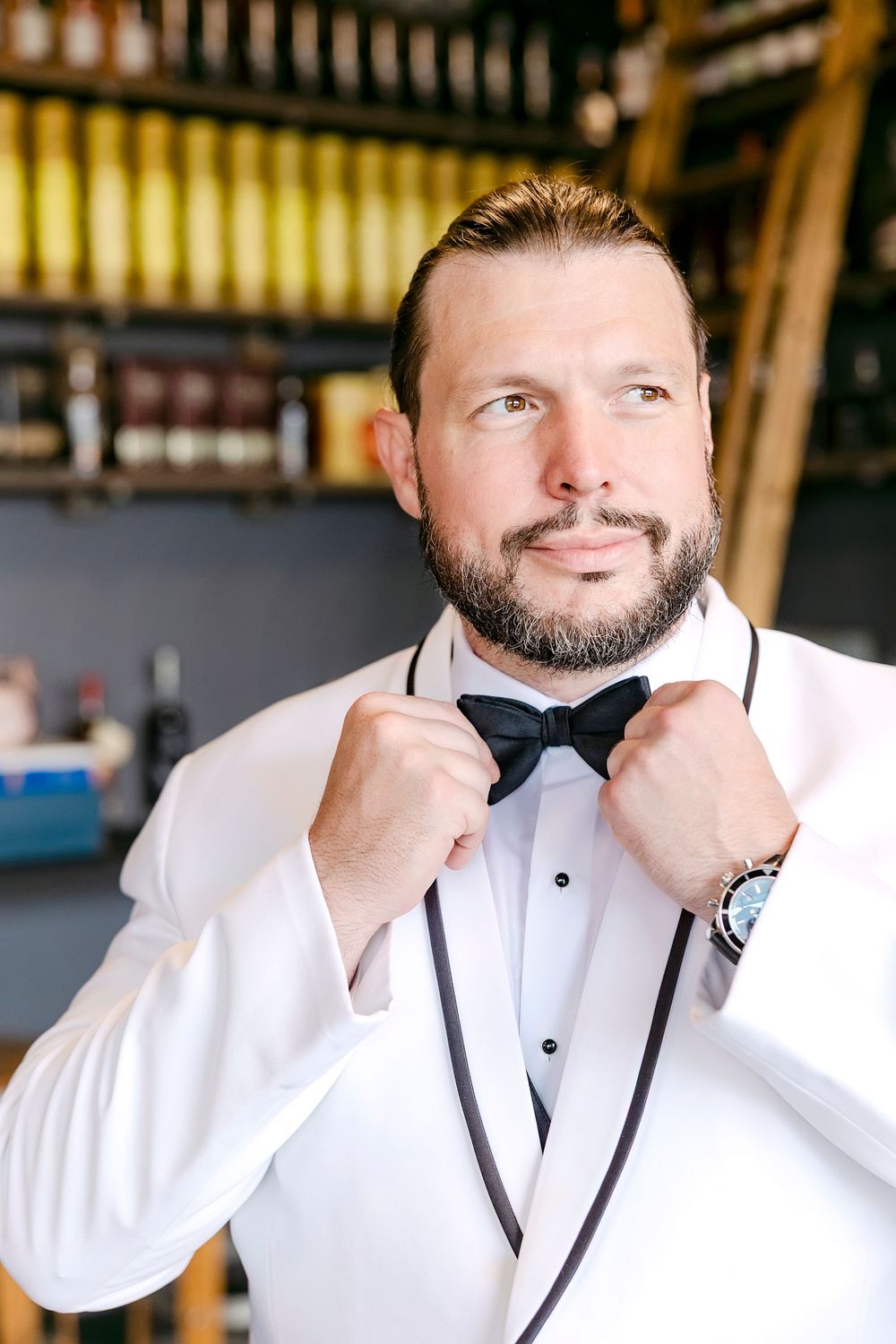 Person in white tuxedo jacket and black bow tie adjusting formal attire.