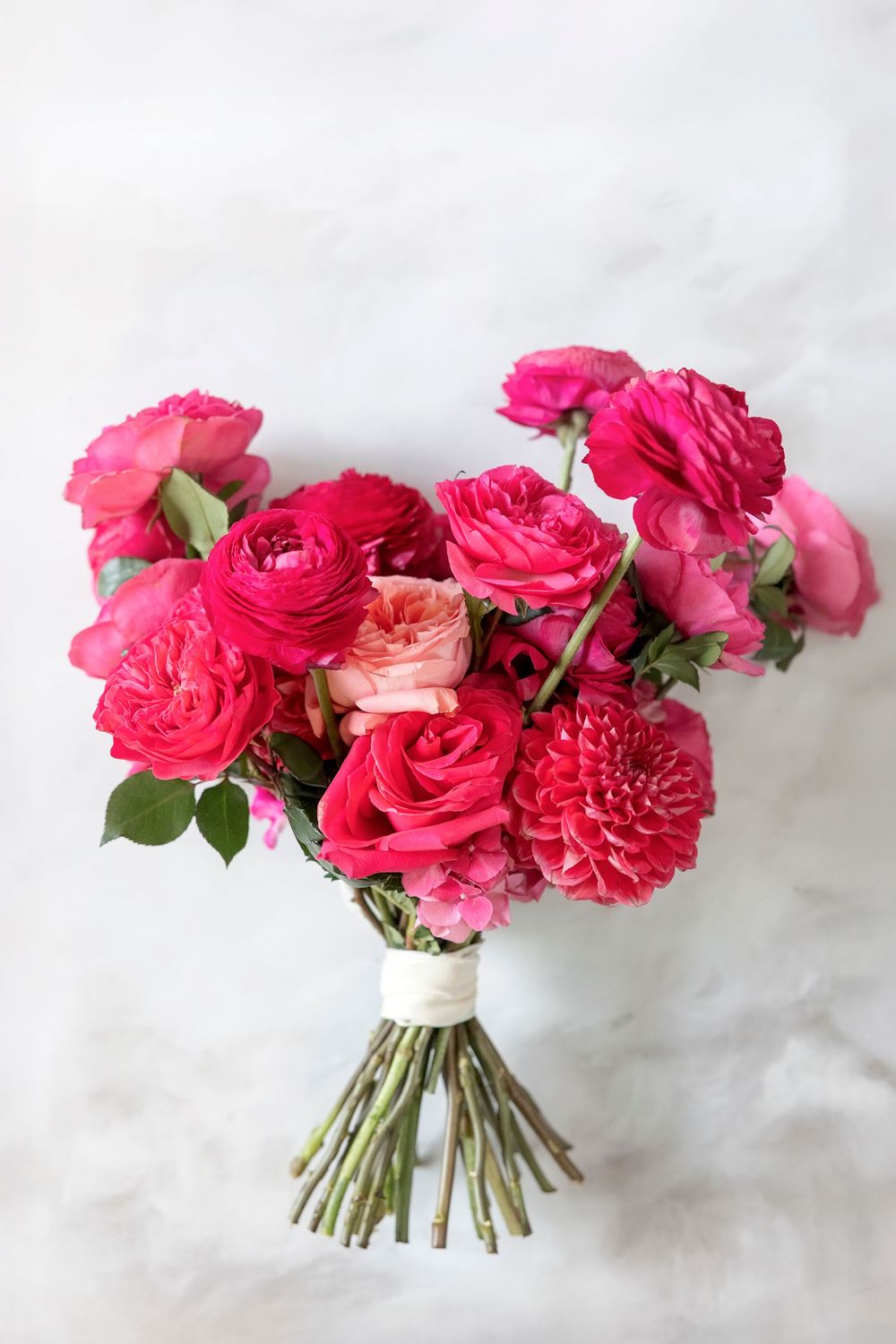 Three identical bouquets of bright pink roses and dahlias arranged against a white marble background.