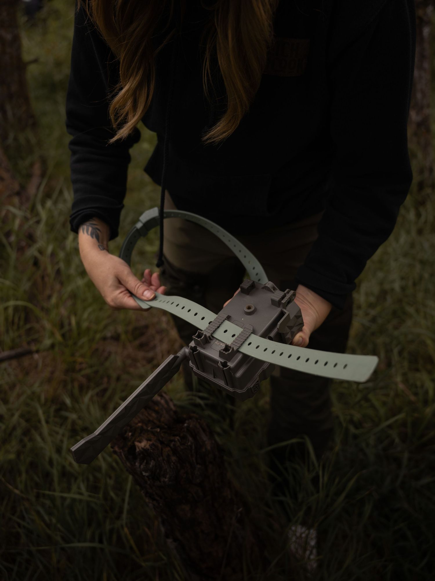 Hands working with gray metal camera mounting brackets in outdoor setting.