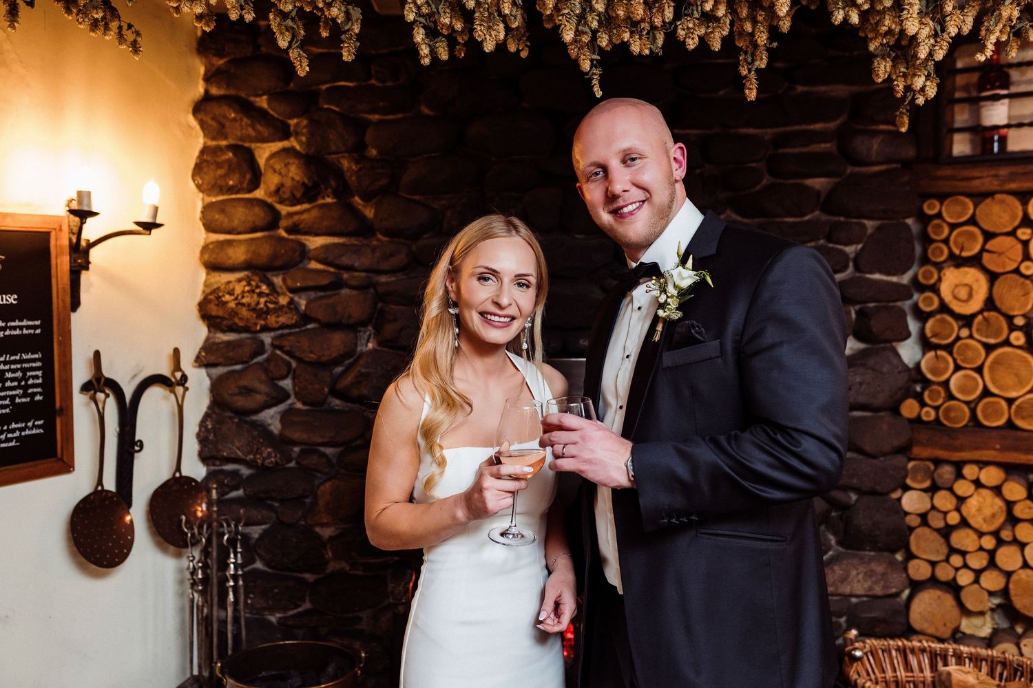 A couple shares a celebratory toast at their rustic wedding reception with stone walls and warm lighting.