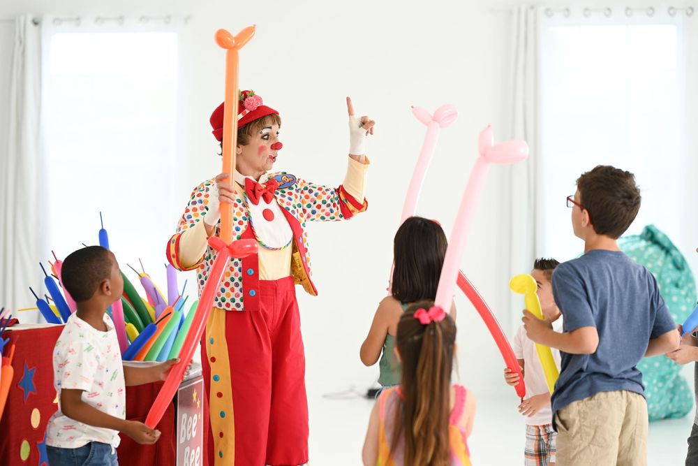 Clown entertainer in red overalls leads children in fun activities with balloon animals.