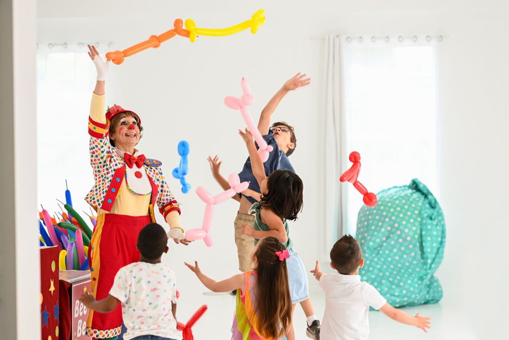 Clown performer and children playing with colorful balloon sculptures during an interactive show.