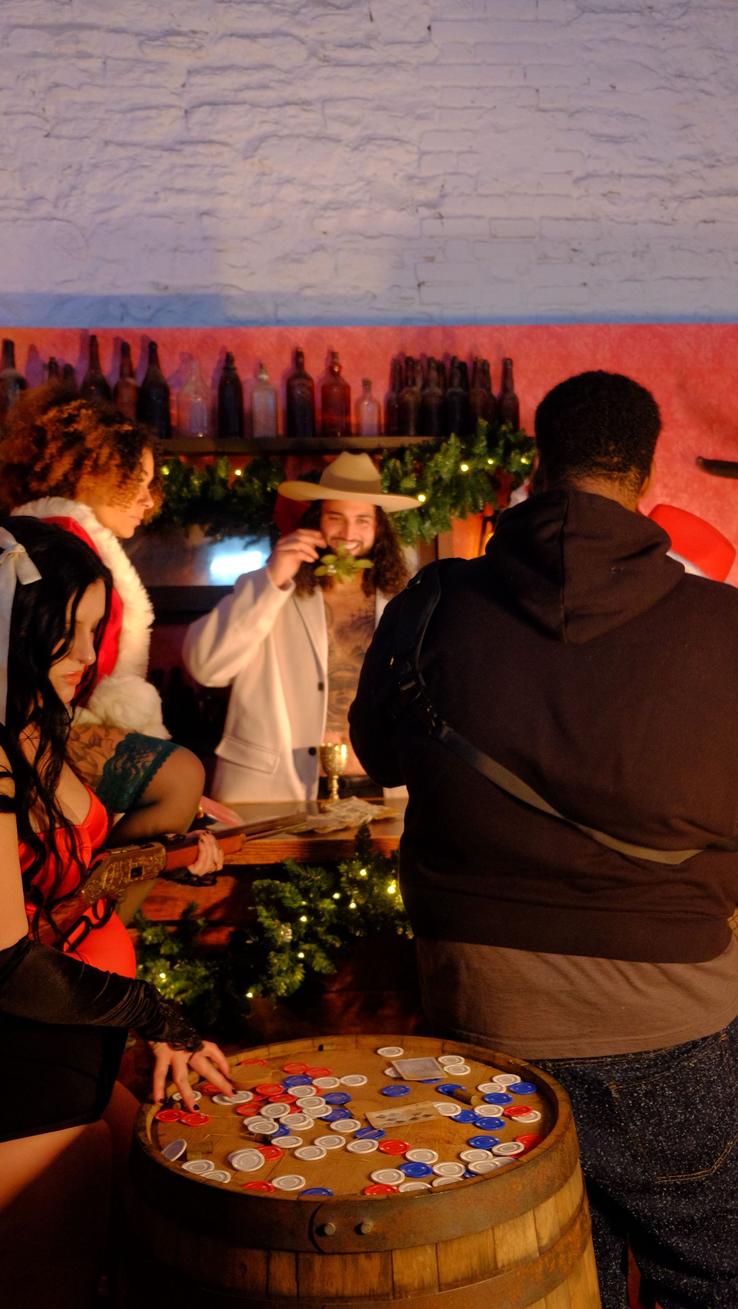 People playing poker on a wooden barrel table with red ambient lighting and poker chips scattered across the surface.