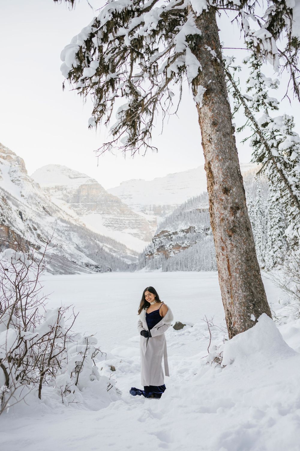 Beautiful bride to be and Snow covered Fairmont Chateau Lake Louise with mountains and frozen lake during winter photoshoot