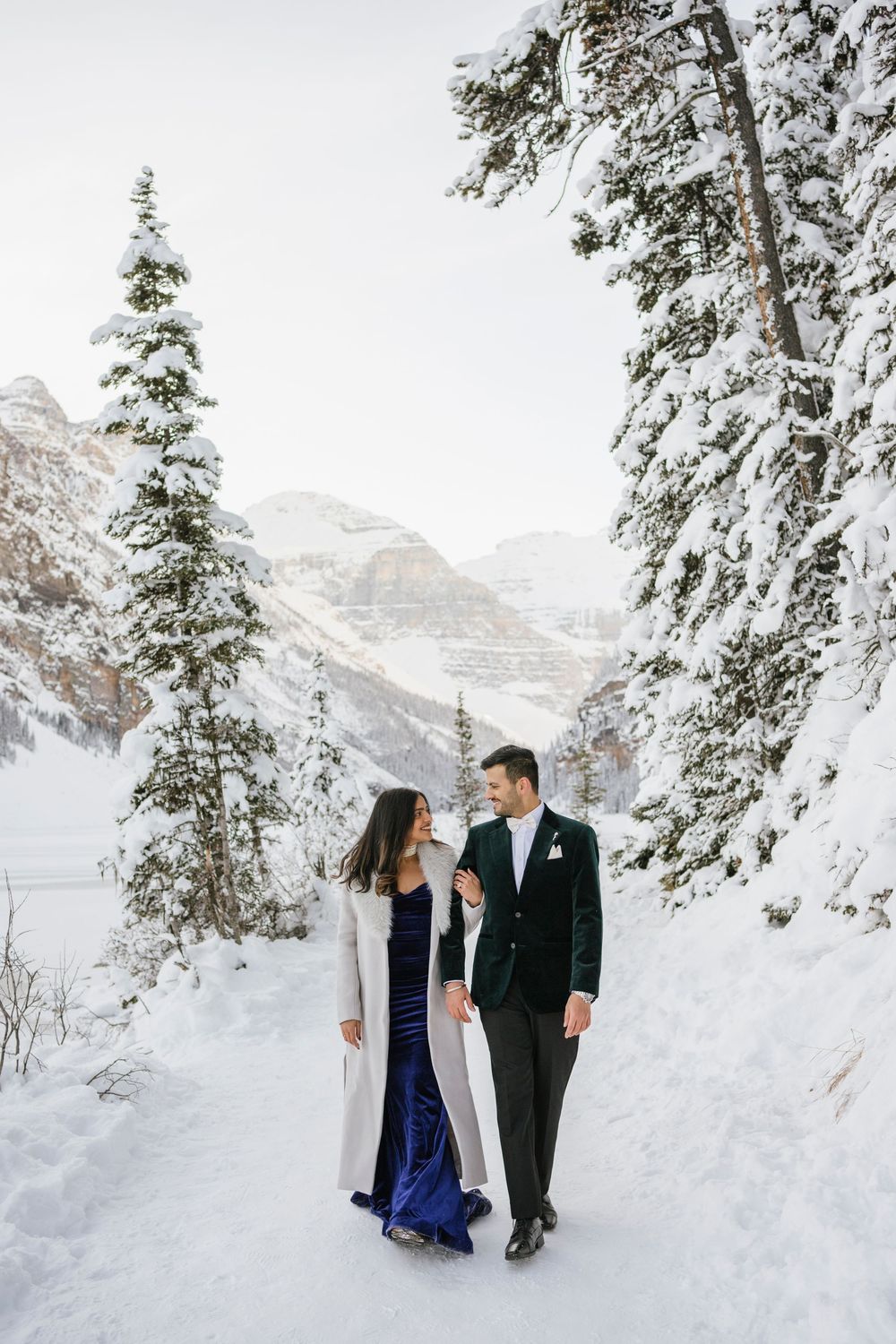 Couple walking hand in hand on frozen Lake Louise with Victoria Glacier in the background, winter engagement photo