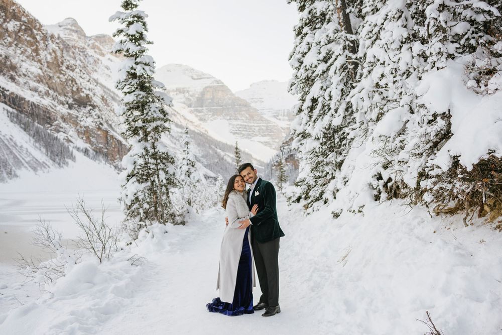 Couple walking hand in hand on frozen Lake Louise with Victoria Glacier in the background, winter engagement photo