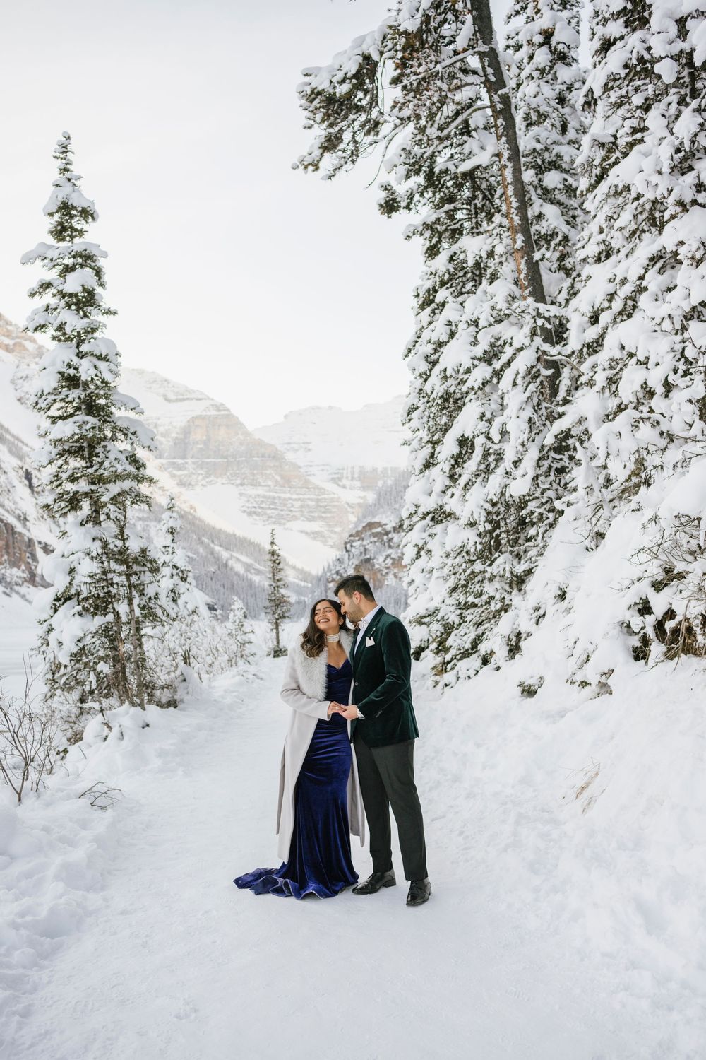 Romantic winter couple portraits on Lake Louise shoreline with soft snow and mountains behind