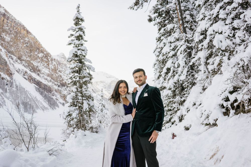 Romantic winter couple portraits on Lake Louise shoreline with soft snow and mountains behind