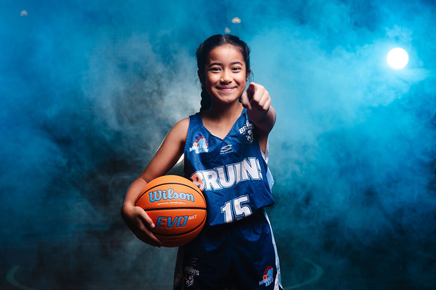 Basketball player in navy blue Bruins uniform poses with ball against dramatic lighting.